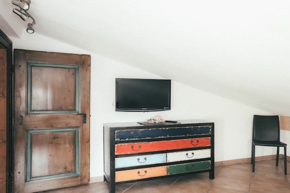 A room with a wooden door, a television mounted on the wall, and a multi-colored dresser with drawers. - Luna Mia Apartment 4 (Schwangau)