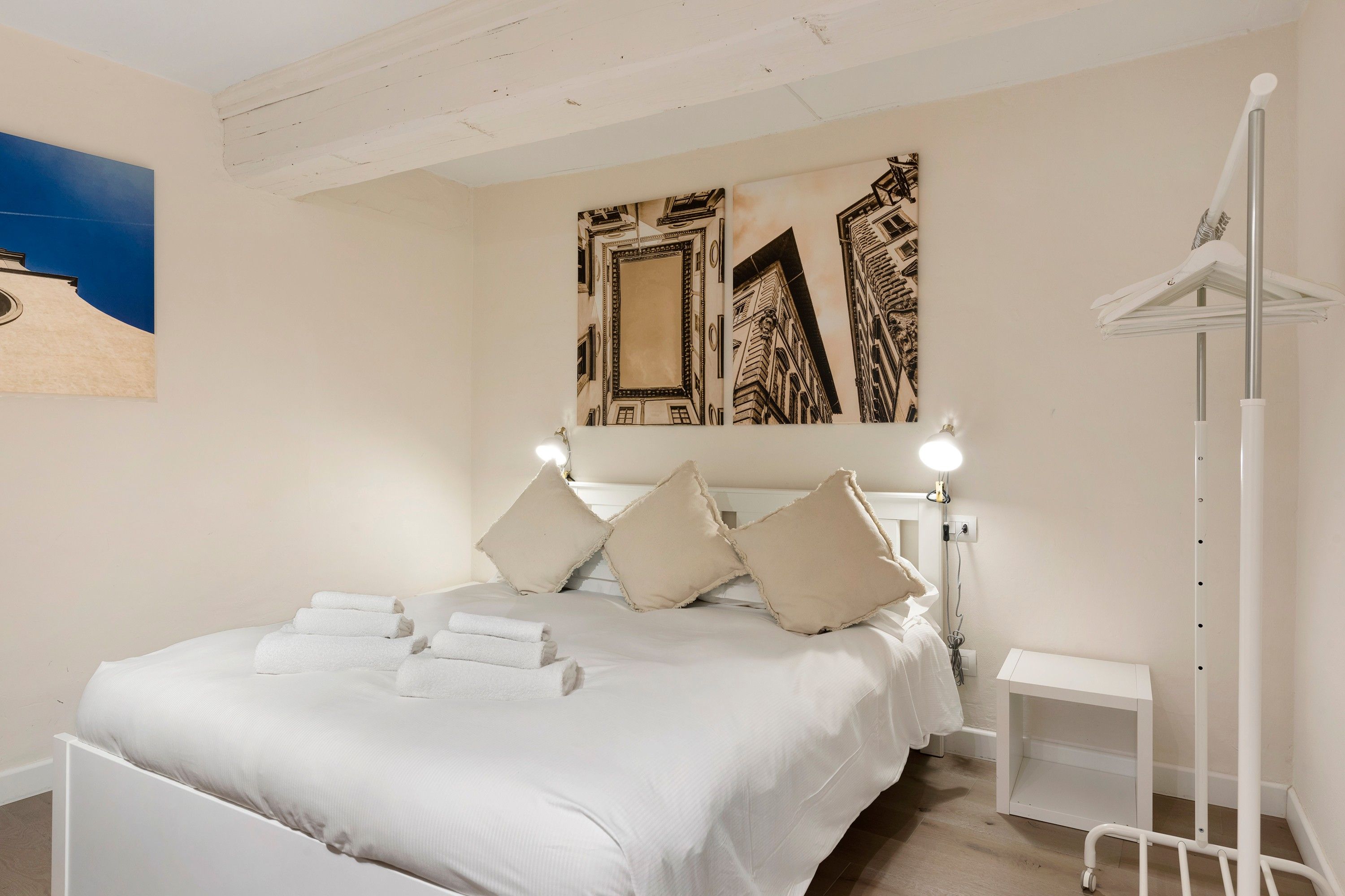 A bedroom with a bed, pillows, a bedside table, and a wall-mounted light fixture.