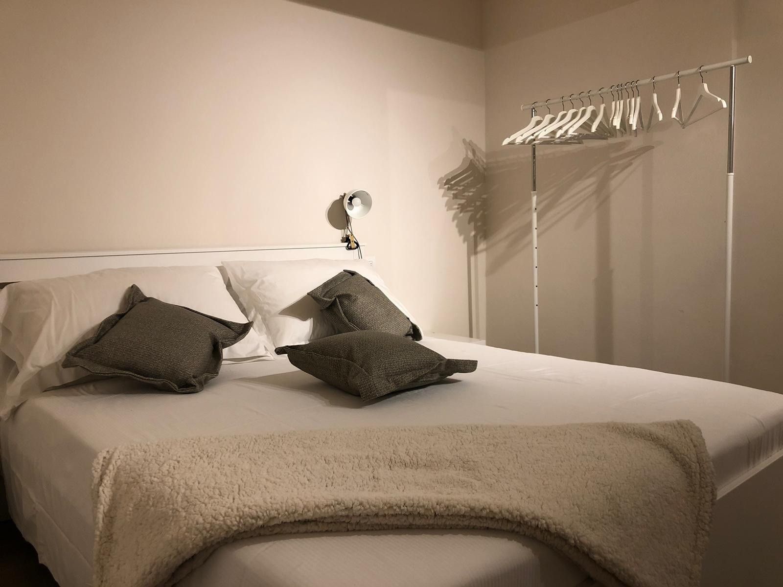 Un lit bien fait, avec des oreillers et une couverture, une lampe de chevet et un portant à vêtements avec des cintres.