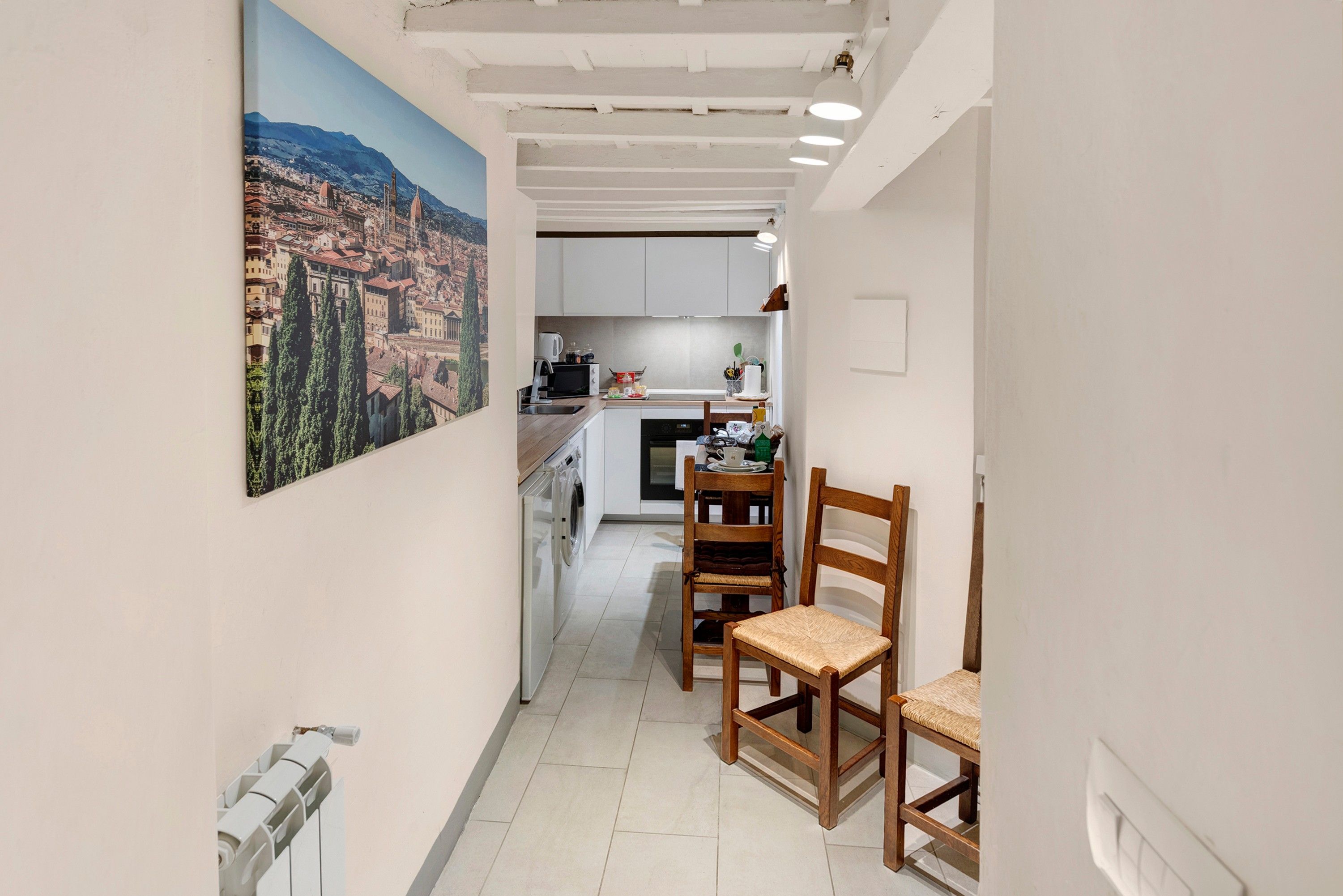 A narrow hallway leading to a kitchen with a view of a cityscape.