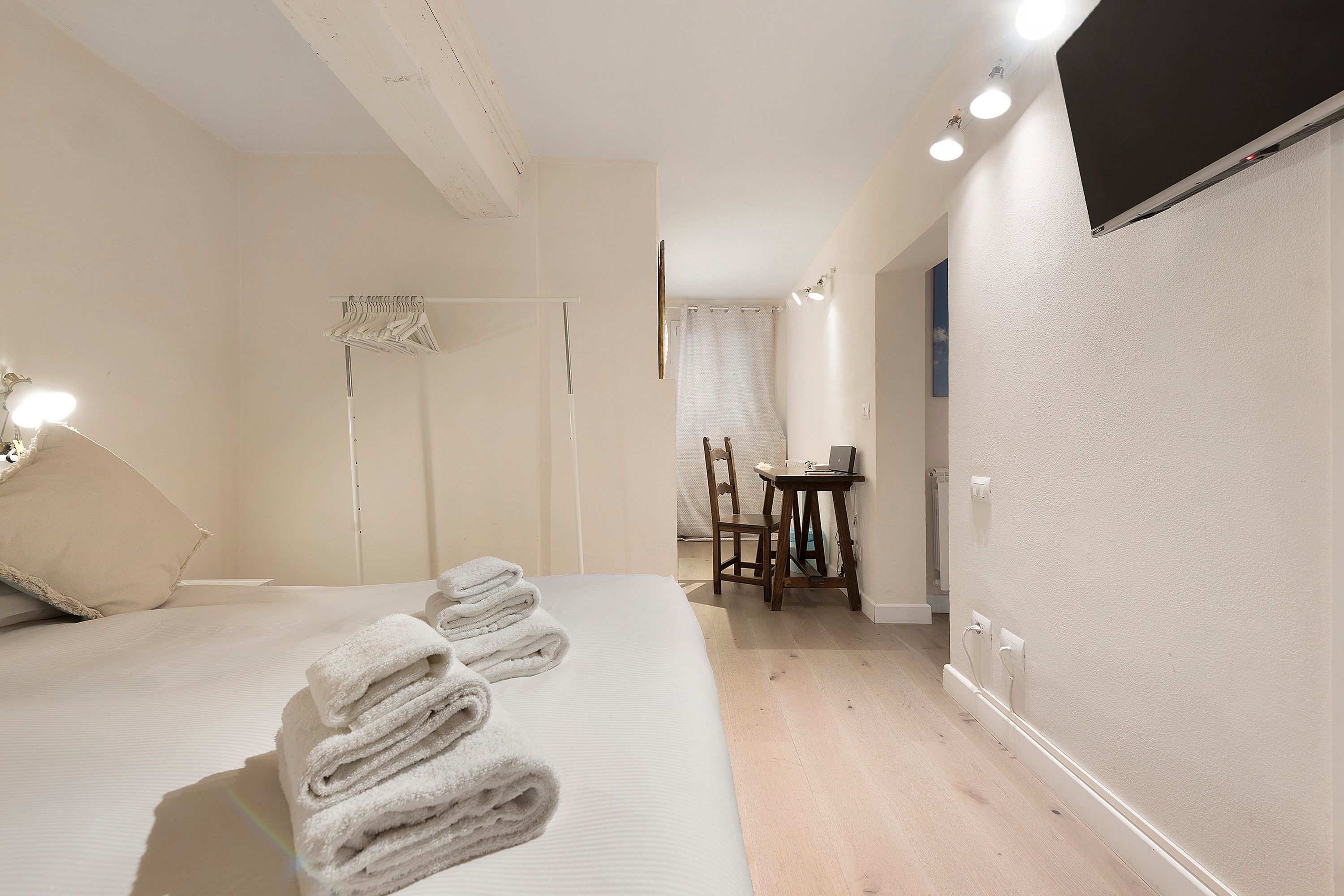 A hotel room with a bed, a desk, and a chair. There are towels on the bed.