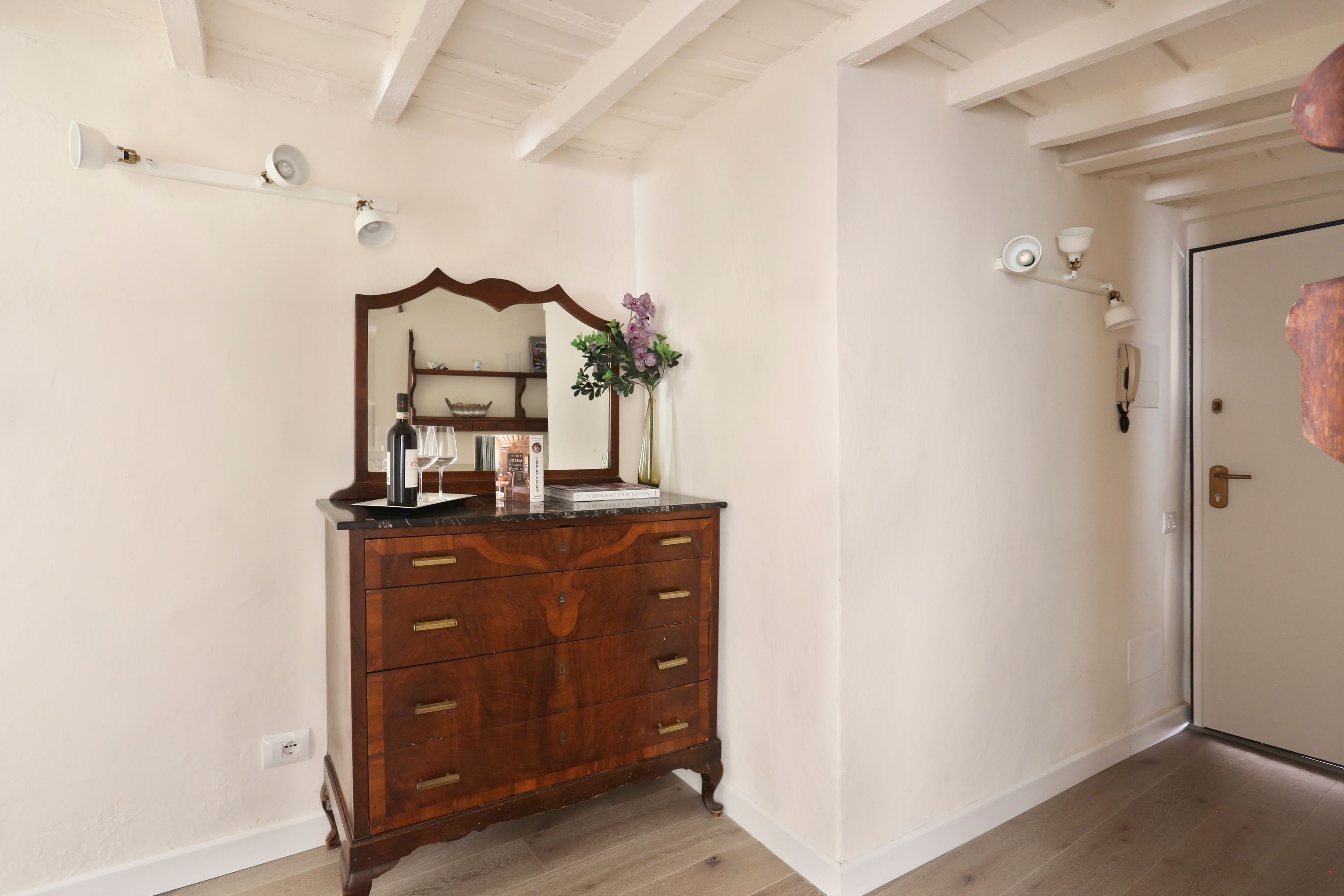 A room with a wooden dresser, a mirror, a vase with flowers, and a door with a keyhole. - Holiday Home 'Alex's House Signoria' with Wi-Fi (Firenze)