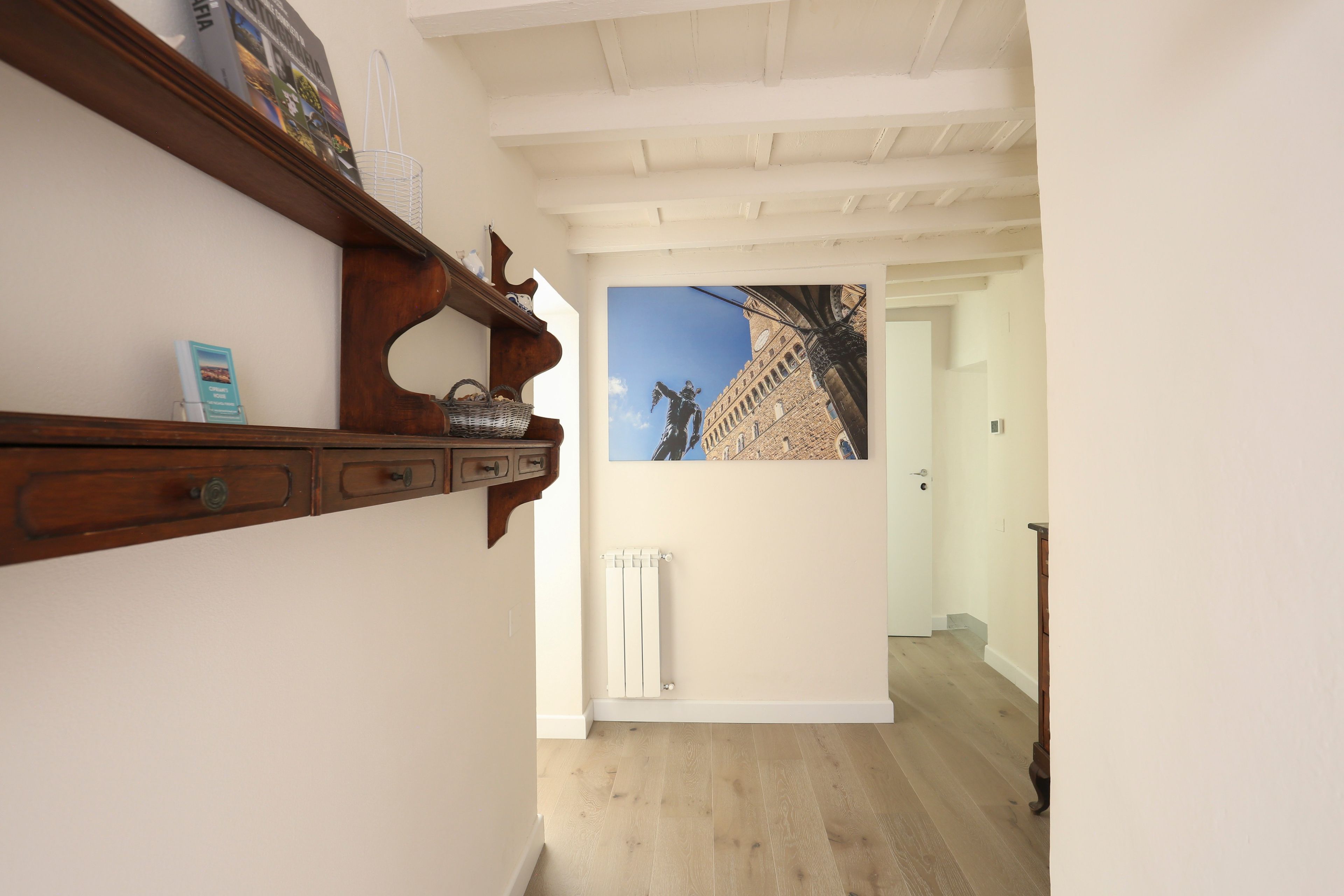 Un couloir avec une étagère en bois, un radiateur et une porte donnant sur une autre pièce.