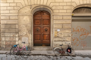 A building with a large wooden double door, two bicycles parked in front, and a garage door with graffiti. - Holiday Home 'Anna's House Ponte Vecchio' with Wi-Fi (Firenze)