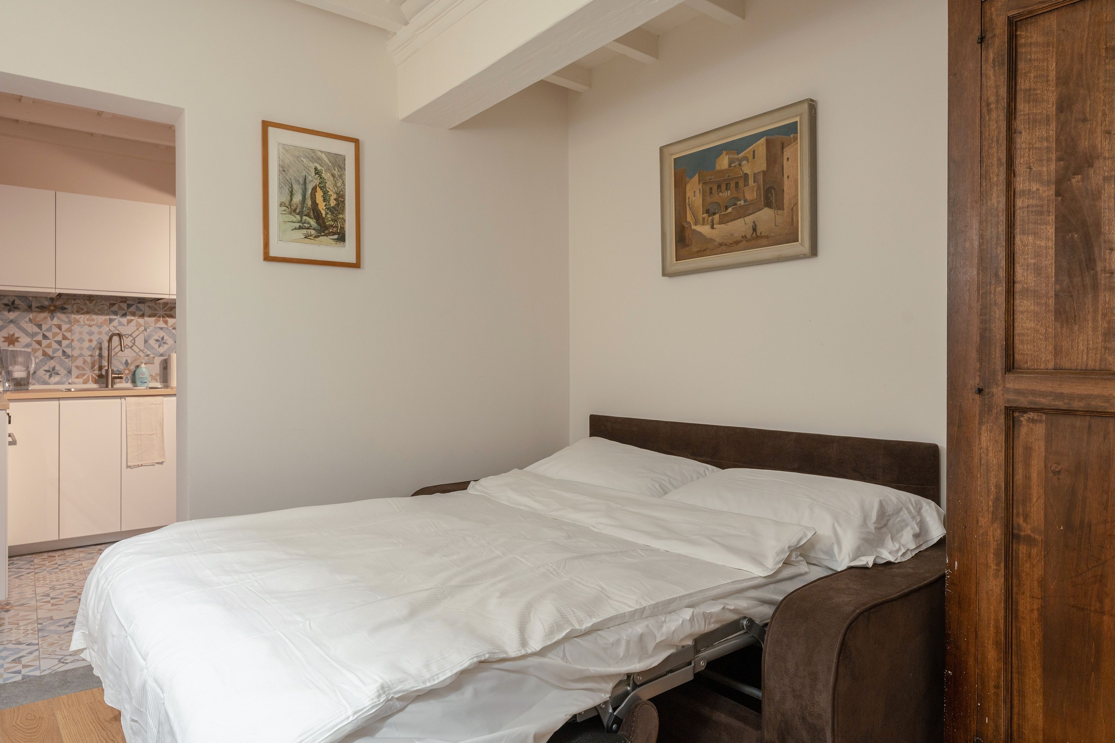 A bedroom with a bed, a wooden wardrobe, and two framed pictures on the wall.