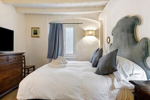 Une chambre à coucher comprenant un lit, une commode, un téléviseur, une fenêtre avec des rideaux et une lampe fixée au mur.