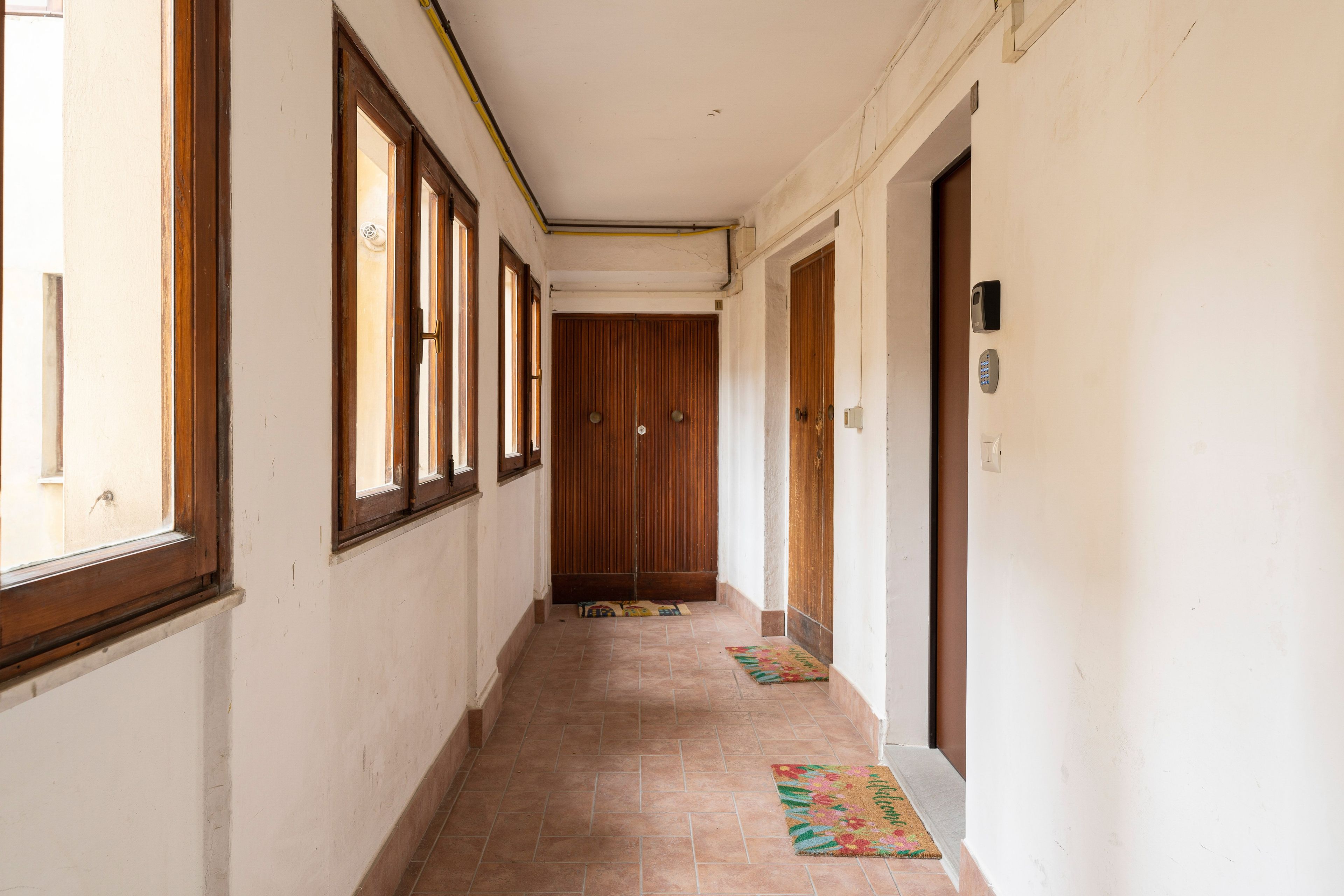 Un couloir avec des portes en bois, un sol carrelé et une fenêtre sur le côté gauche.