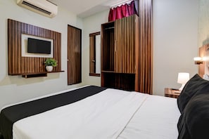 A hotel room with a bed, a TV mounted on the wall, a small plant, and a nightstand with a lamp. - OYO Hotel Blue Sapphire Residency Near (Mumbai)