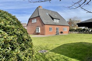 A brick house with a sloped roof, a well-maintained lawn, and a stone wall in the background. - Holiday apartment in Sylt with swimming pool (Sylt)