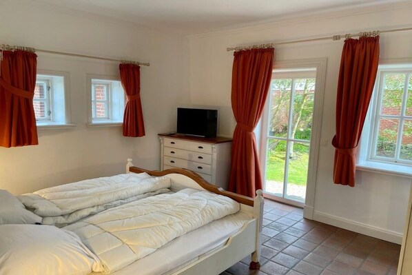 A bedroom with a bed, a television, and a window with curtains. - Holiday apartment in Sylt with swimming pool (Sylt)