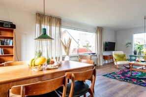 A dining area with a wooden table, chairs, a green pendant light, and a view of the outside through large windows. - Uthland on the beach (Sylt)