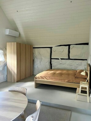 Une chambre moderne avec un plafond en pente, un lit avec une tête de lit, une petite table et une chaise.