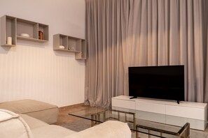 Una sala de estar moderna con un televisor de pantalla plana sobre un mueble blanco, sofás color beige y una mesa de centro de vidrio.