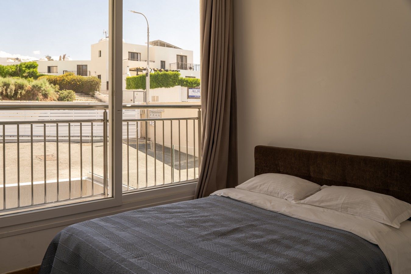 Un dormitorio con cama, ventana con vista a un edificio y calle, y cortina.