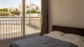 Un dormitorio con cama, ventana con vista a un edificio y calle, y cortina.