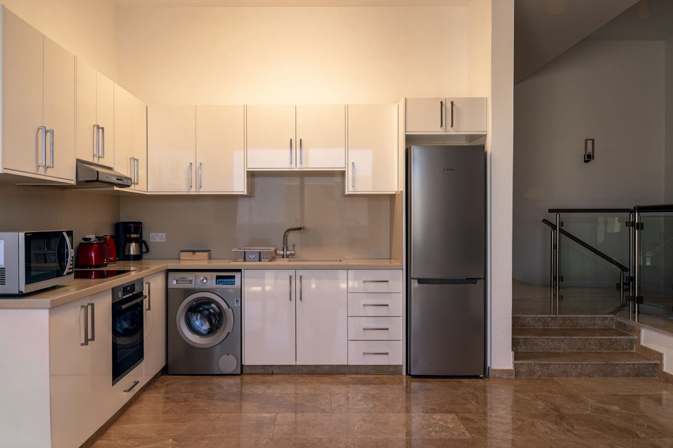 Een moderne keuken met roestvrijstalen apparatuur, een wasmachine en een koelkast.