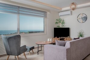 Ein stilvolles Wohnzimmer mit Sofa, Sessel, Fernseher und einem kleinen Tisch.