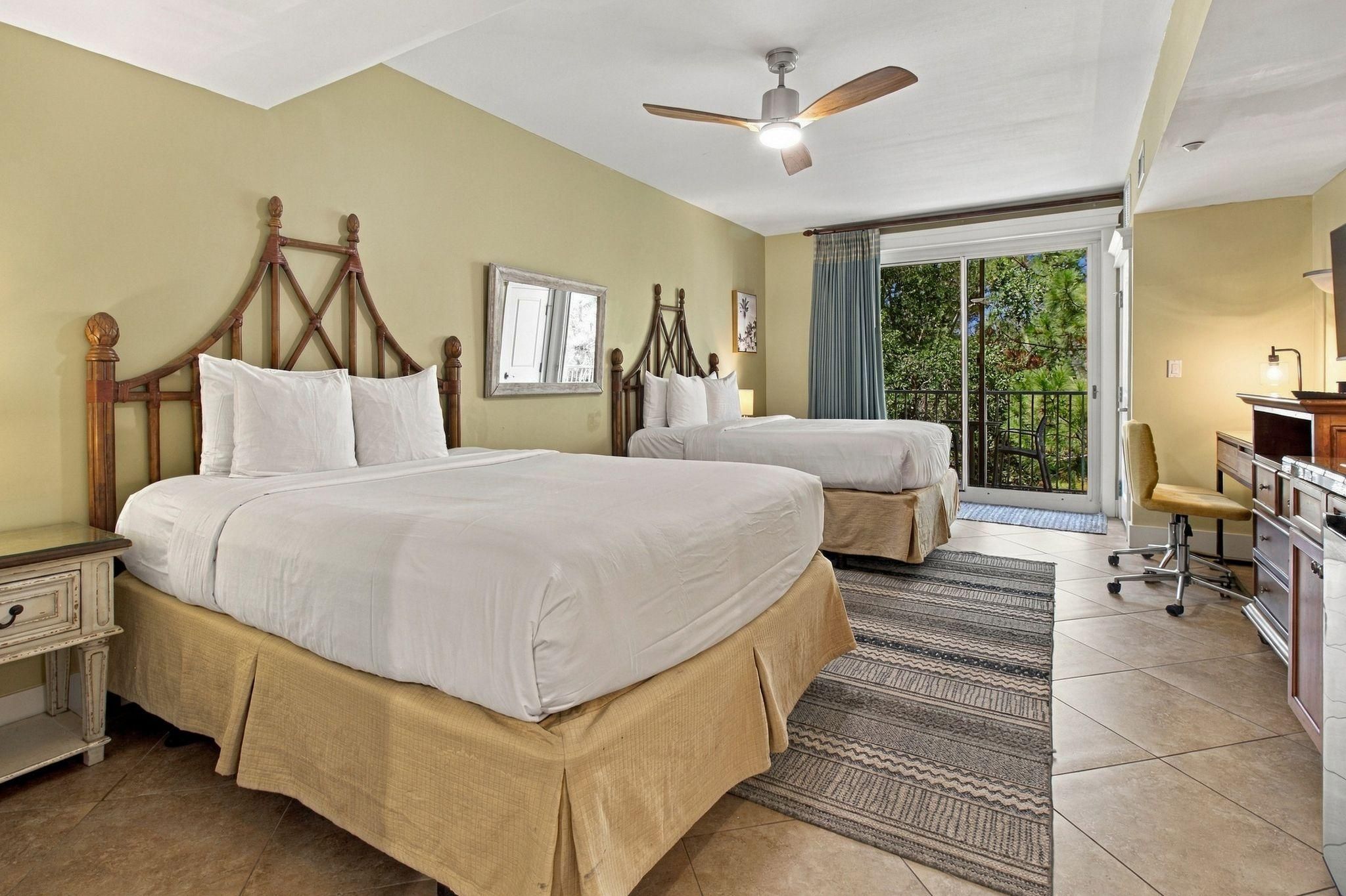 Une chambre d’hôtel avec deux lits, un bureau, une chaise, un ventilateur de plafond et une vue sur l’extérieur.