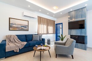 A modern living room with a sofa, armchair, coffee table, and a fireplace. - Serenity Villa Thalassa (Rhodes)