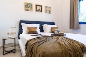 A hotel room with a bed, bedside tables, a window with curtains, and wall art. - Serenity Villa Thalassa (Rhodes)