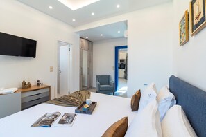 A modern bedroom with a bed, bedside table, and a flat-screen TV. - Serenity Villa Thalassa (Rhodes)