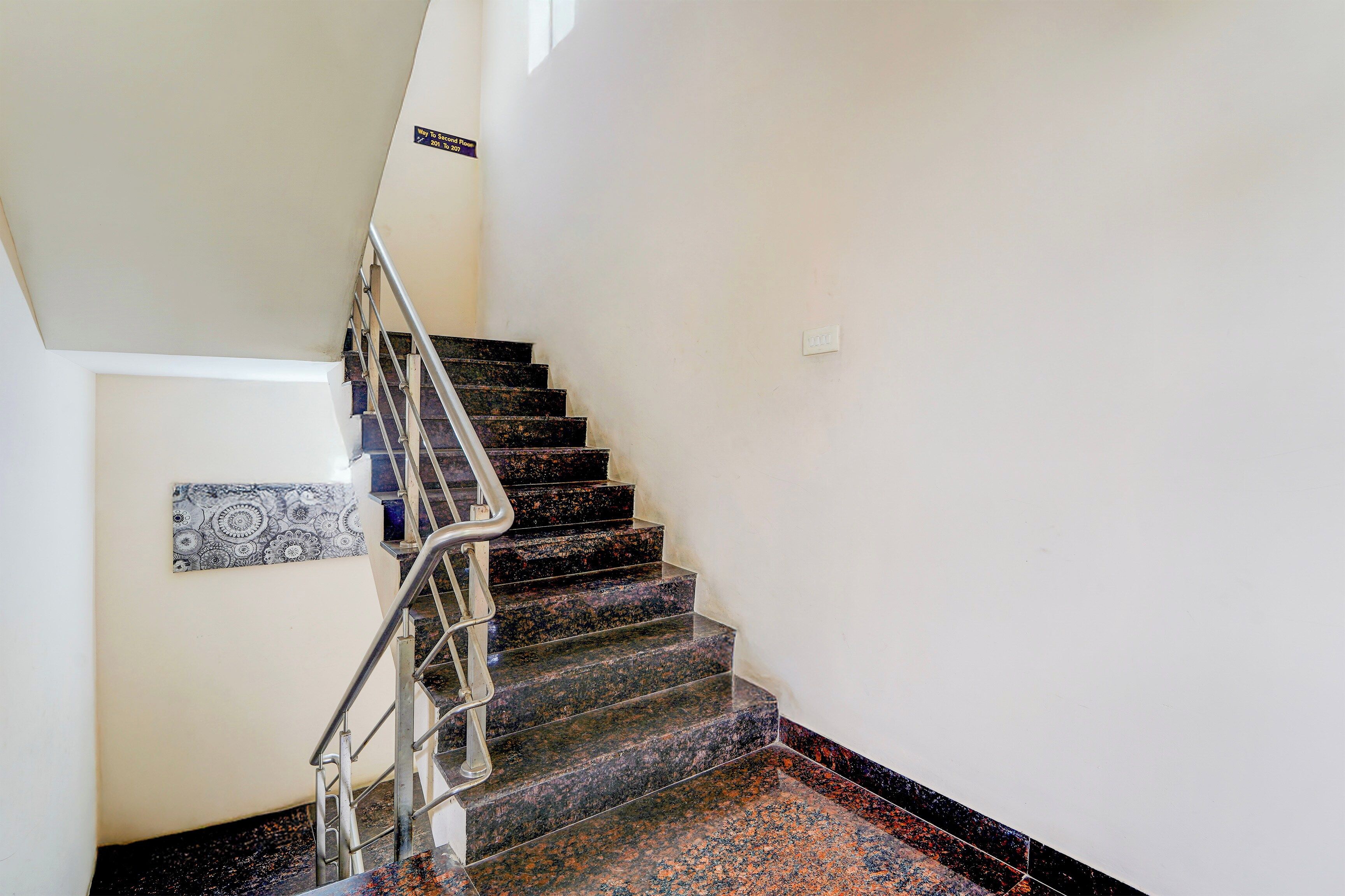 Una escalera con barandilla metálica y un cartel en la pared que indica los números de habitación.