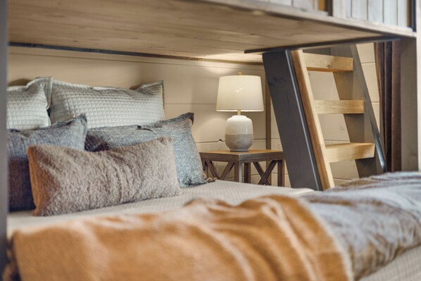 A bed with multiple pillows, a bedside table with a lamp, and a wooden ladder leaning against the wall. - Private Indoor Pool | Arcade Loft & Hot Tub (Sevierville)