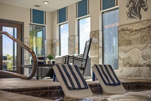A hot tub area with two lounge chairs, a table, and a window with a view. - Private Indoor Pool | Arcade Loft & Hot Tub (Sevierville)