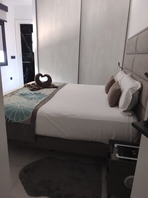 Ein Schlafzimmer mit Bett, Kissen, einer herzförmigen Dekoration, einem Nachttisch und einer kleinen Schublade.
