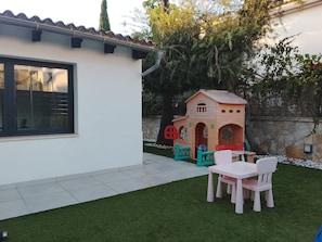 Ein Haus mit Terrasse, Spielhaus und einem kleinen Tisch mit Stühlen.