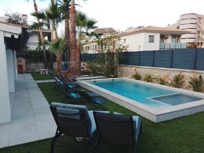 Ein Schwimmbecken mit Liegestühlen, Palmen und einer Steinmauer.