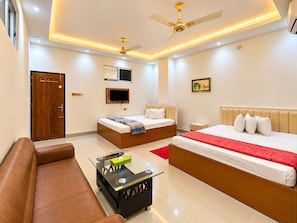 A hotel room with a bed, a sofa, a TV, a ceiling fan, and a window.