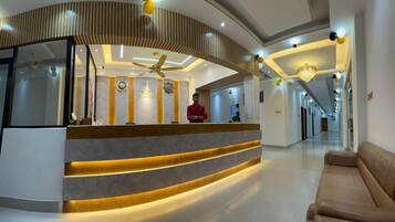 A hotel reception area with a curved reception desk, a ceiling fan, and a chandelier.