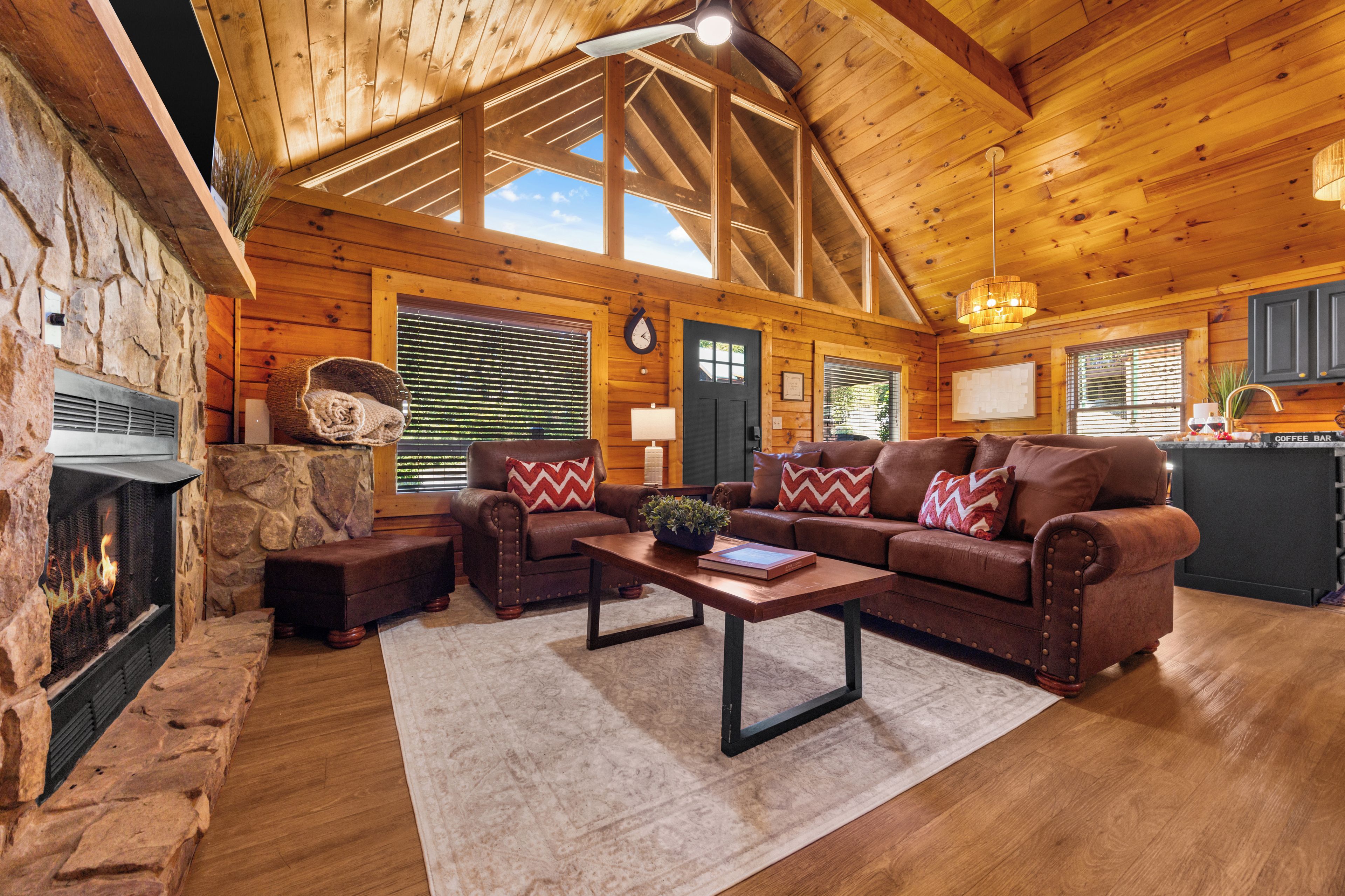 A cozy log cabin interior with a stone fireplace, leather sofas, and a coffee bar.