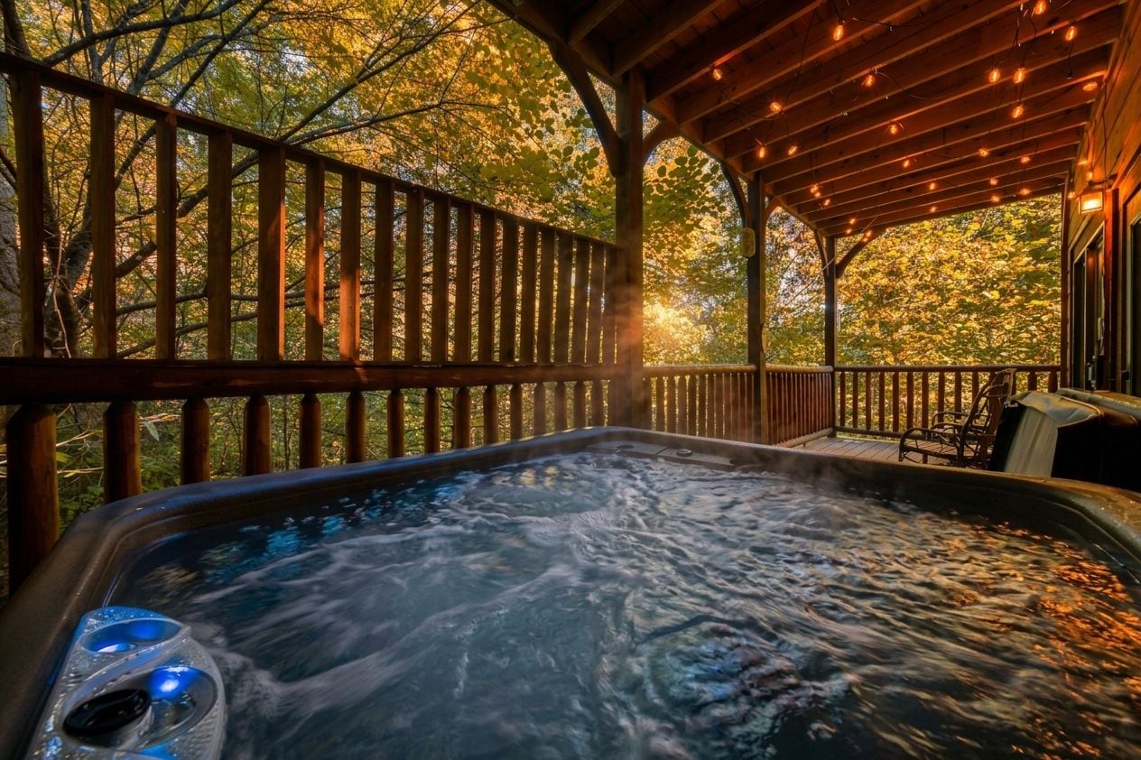 A hot tub with a wooden deck and railing, surrounded by trees.