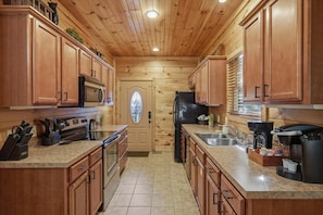 A compact kitchen with wooden cabinets, stainless steel appliances, and a tiled floor. - Sleeps 10, Dog Friendly, Hot Tub, Arcade, Pool Table, 2.5 Mi to Gatlinburg (Gatlinburg)