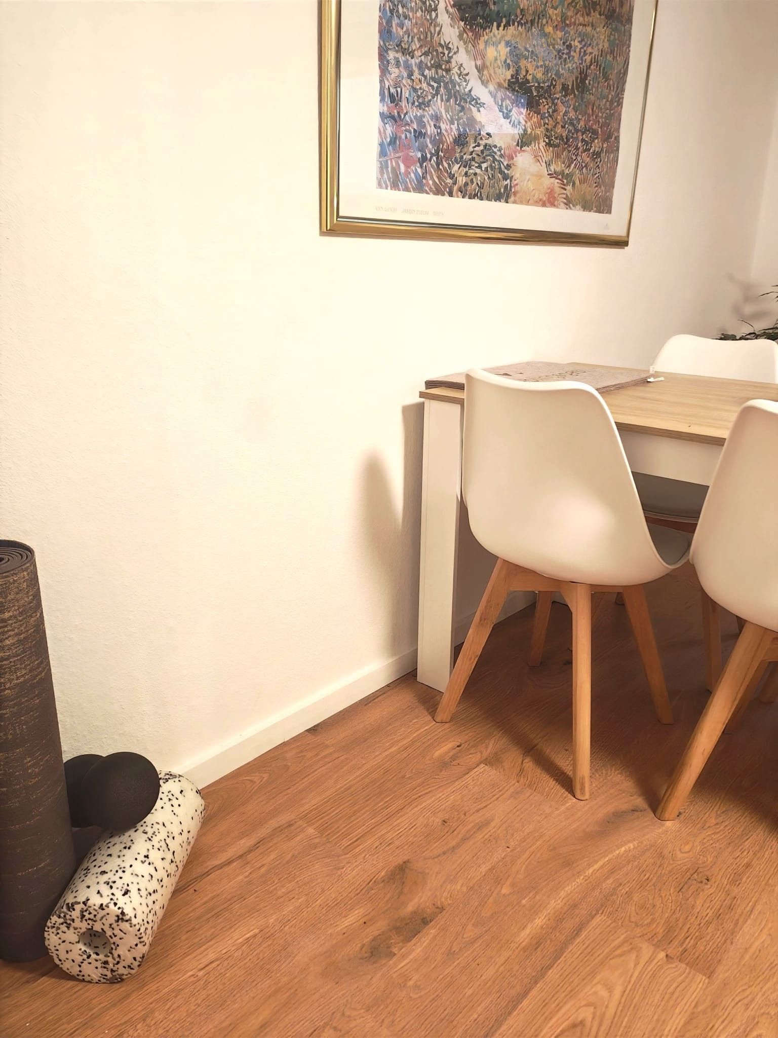 A dining area with a wooden table, white chairs, and a framed artwork on the wall.