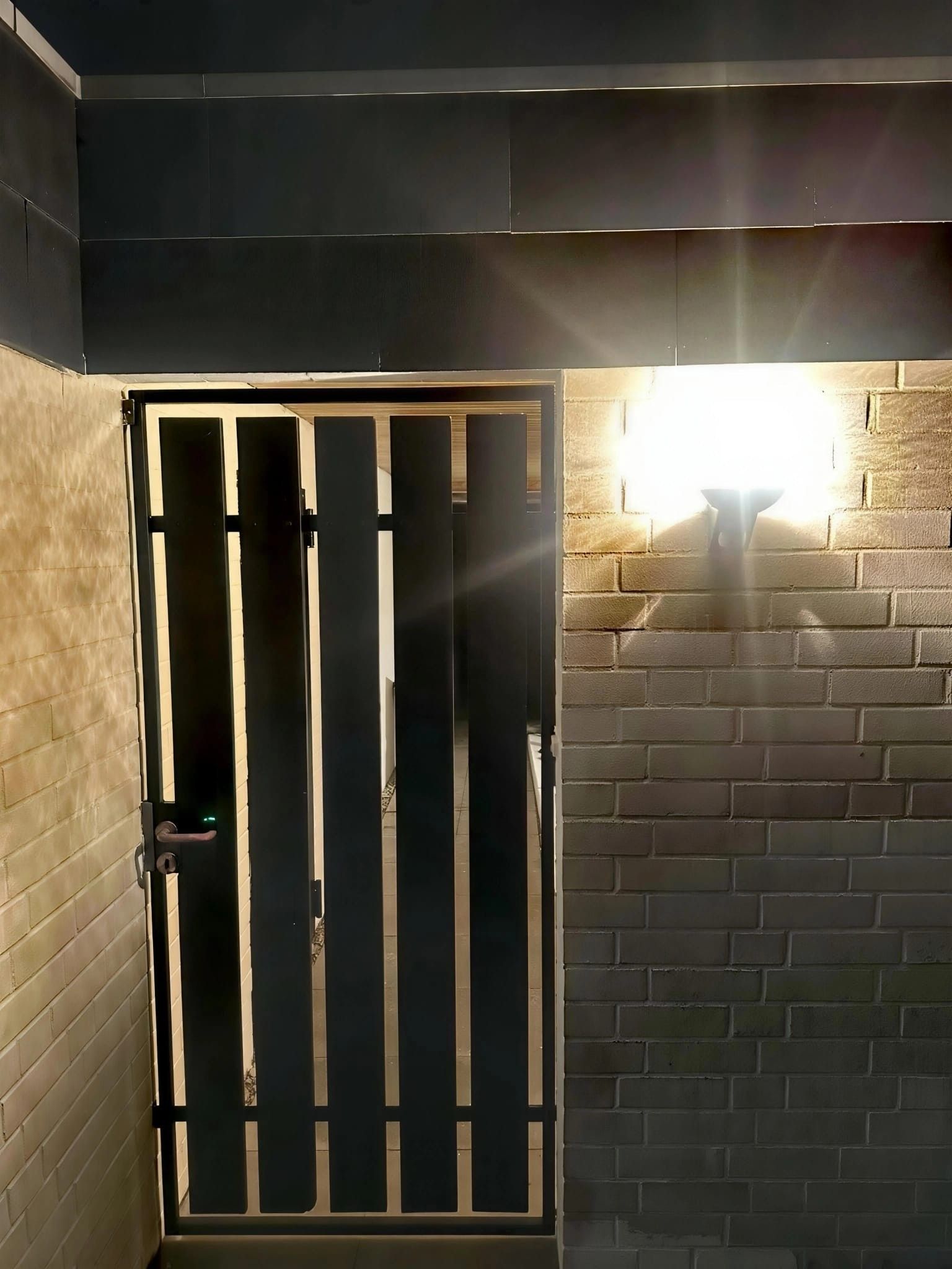A gated entrance with a metal gate and a wall-mounted light fixture.