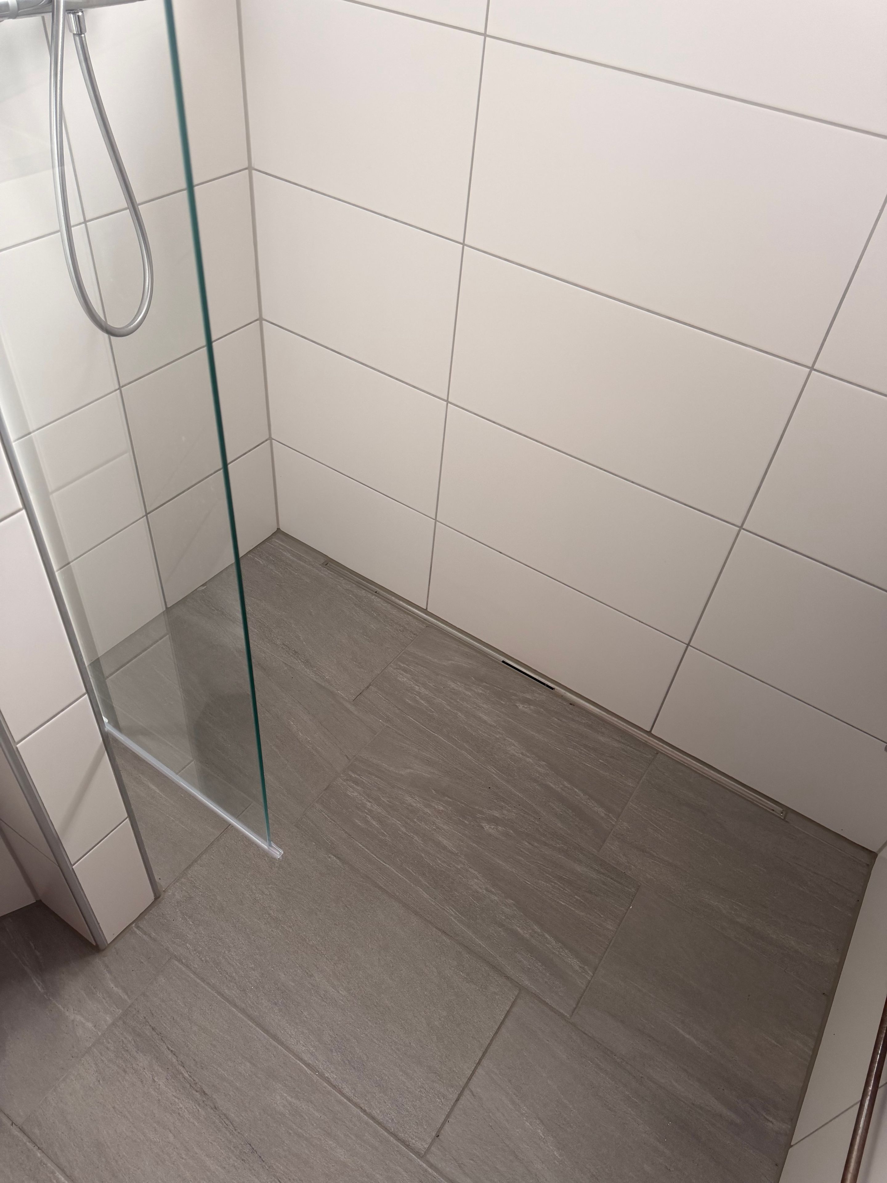 Ein Duschbereich mit Glaswand, gefliesten Wänden und Holzboden.