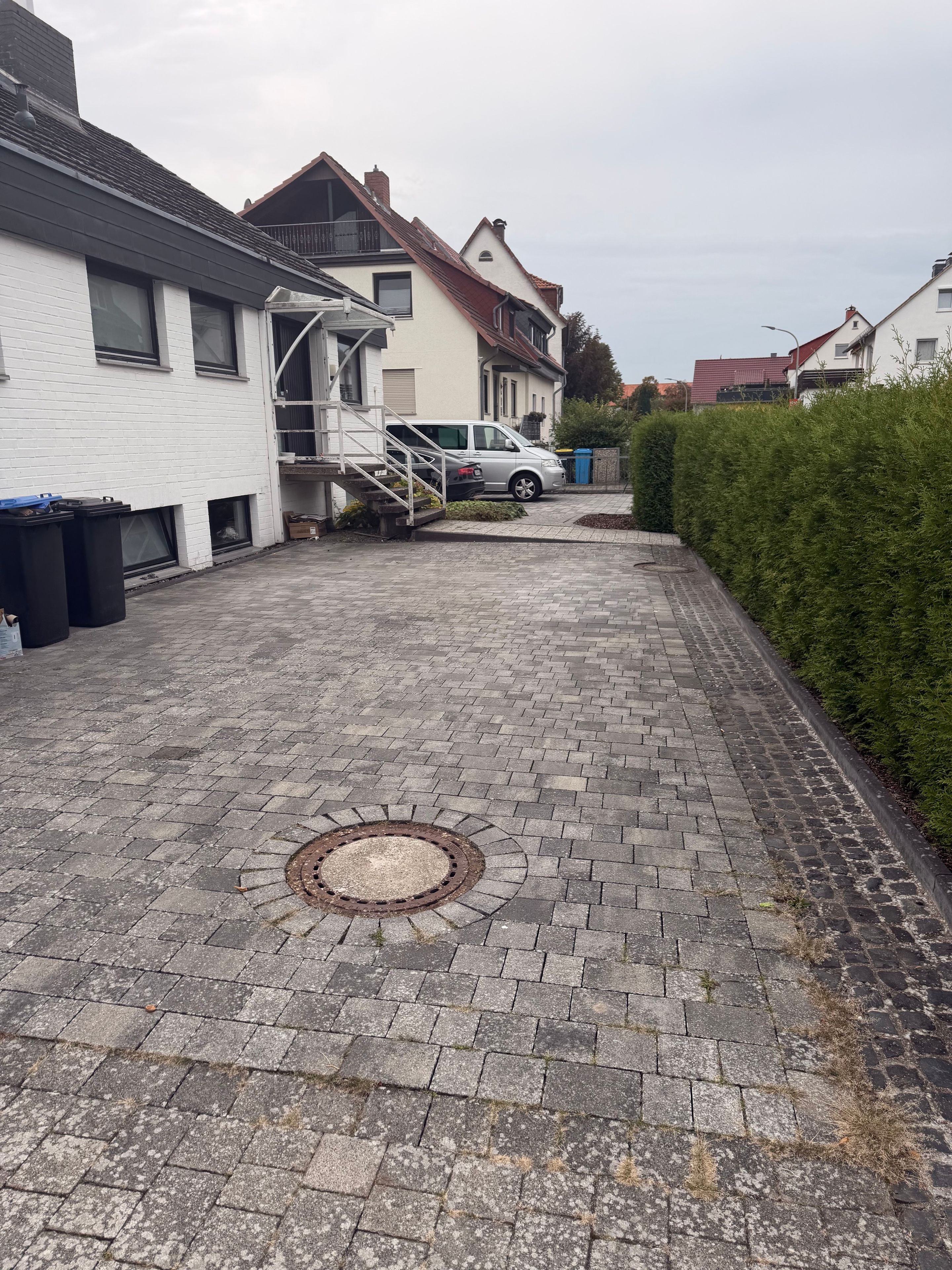 A residential street with a paved walkway, a manhole cover, and houses with balconies.