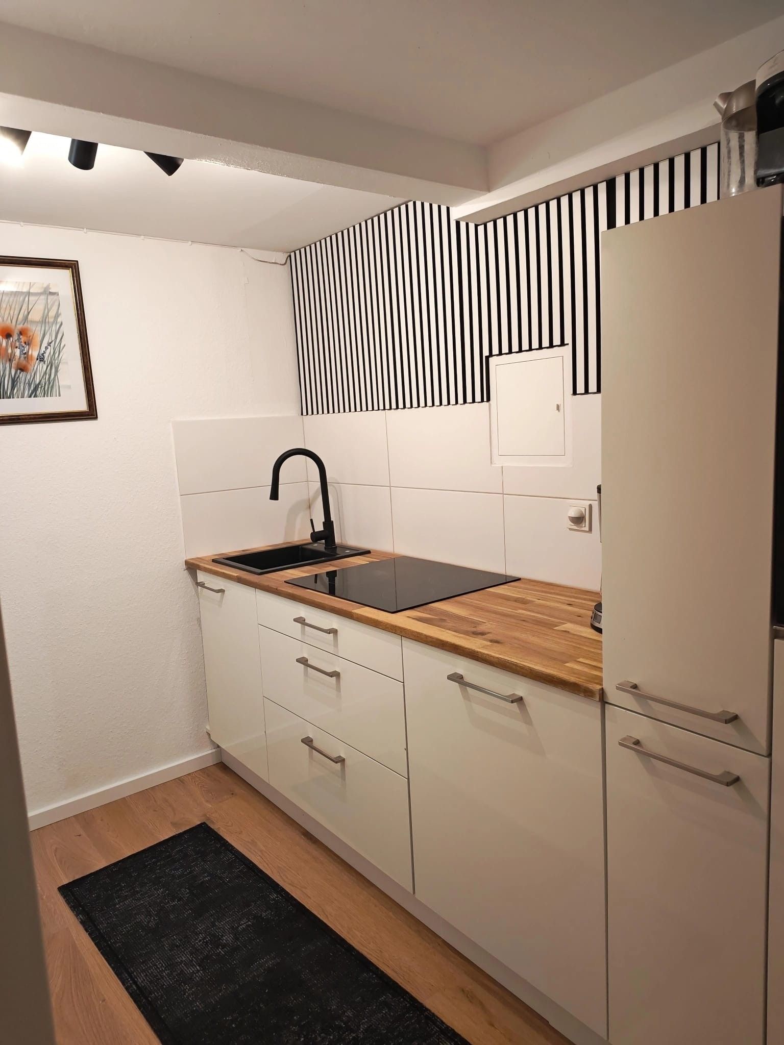 A compact kitchen with white cabinets, a black sink, and a wooden countertop.