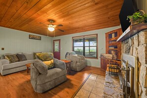 A cozy living room with a wooden ceiling, a fireplace, a sofa, a chair, and a window with a view of the outdoors. - Sleeps 6, Mountain View Hot Tub, Sunset Deck, Single Level, Fireplace (Sevierville)