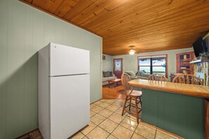 A compact kitchen with a white refrigerator, wooden ceiling, and a dining area with a table and chairs. - Sleeps 6, Mountain View Hot Tub, Sunset Deck, Single Level, Fireplace (Sevierville)