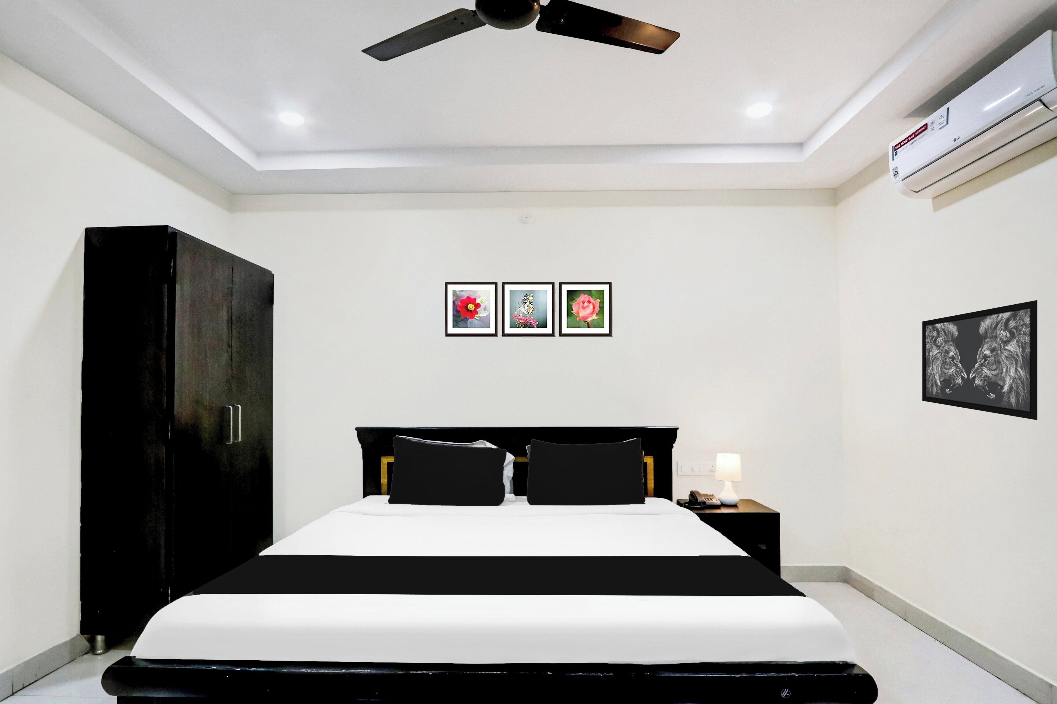 A hotel room with a bed, a wardrobe, a ceiling fan, an air conditioning unit, and three framed pictures on the wall.
