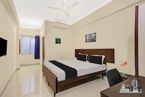 Habitación de hotel con cama, escritorio con hervidor, silla, ventana con cortinas y ventilador de techo.