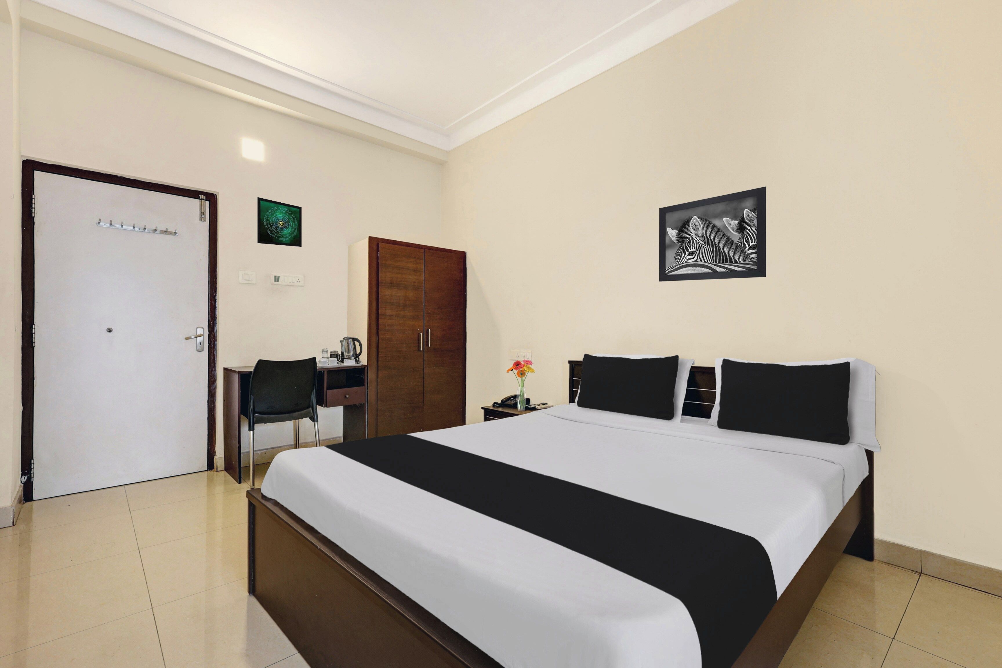 A hotel room with a bed, a desk, a chair, a wardrobe, and a wall-mounted picture.