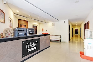Zona de recepción de un hotel con mostrador, dispensador de agua, banca y un pasillo que da a otras habitaciones.