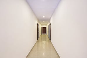 A long, narrow hallway with a shiny tiled floor and white walls. - Super OYO Collection O jagadamba (Visakhapatnam)