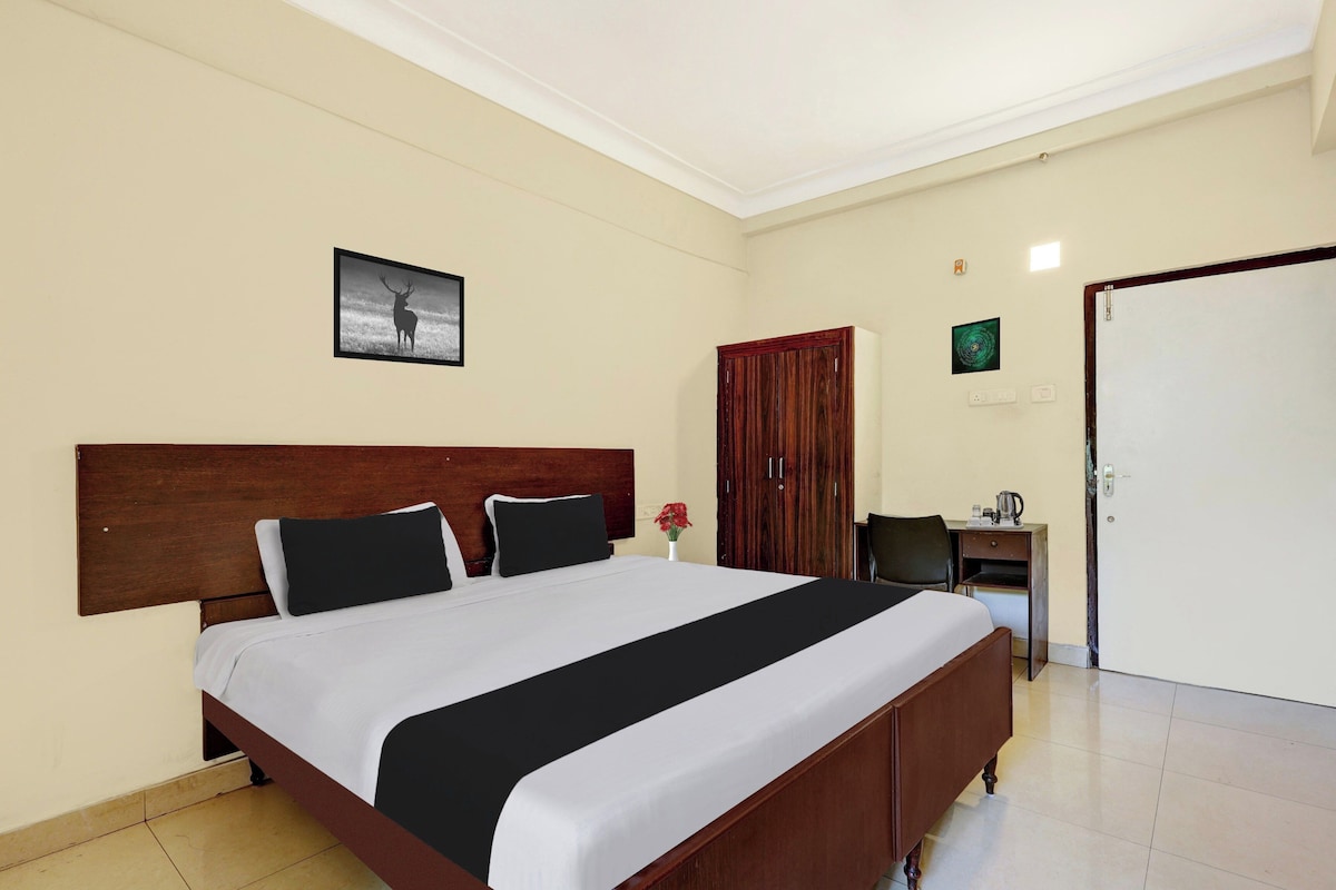A hotel room with a large bed, a wooden headboard, a desk with a chair, a wardrobe, and a door.