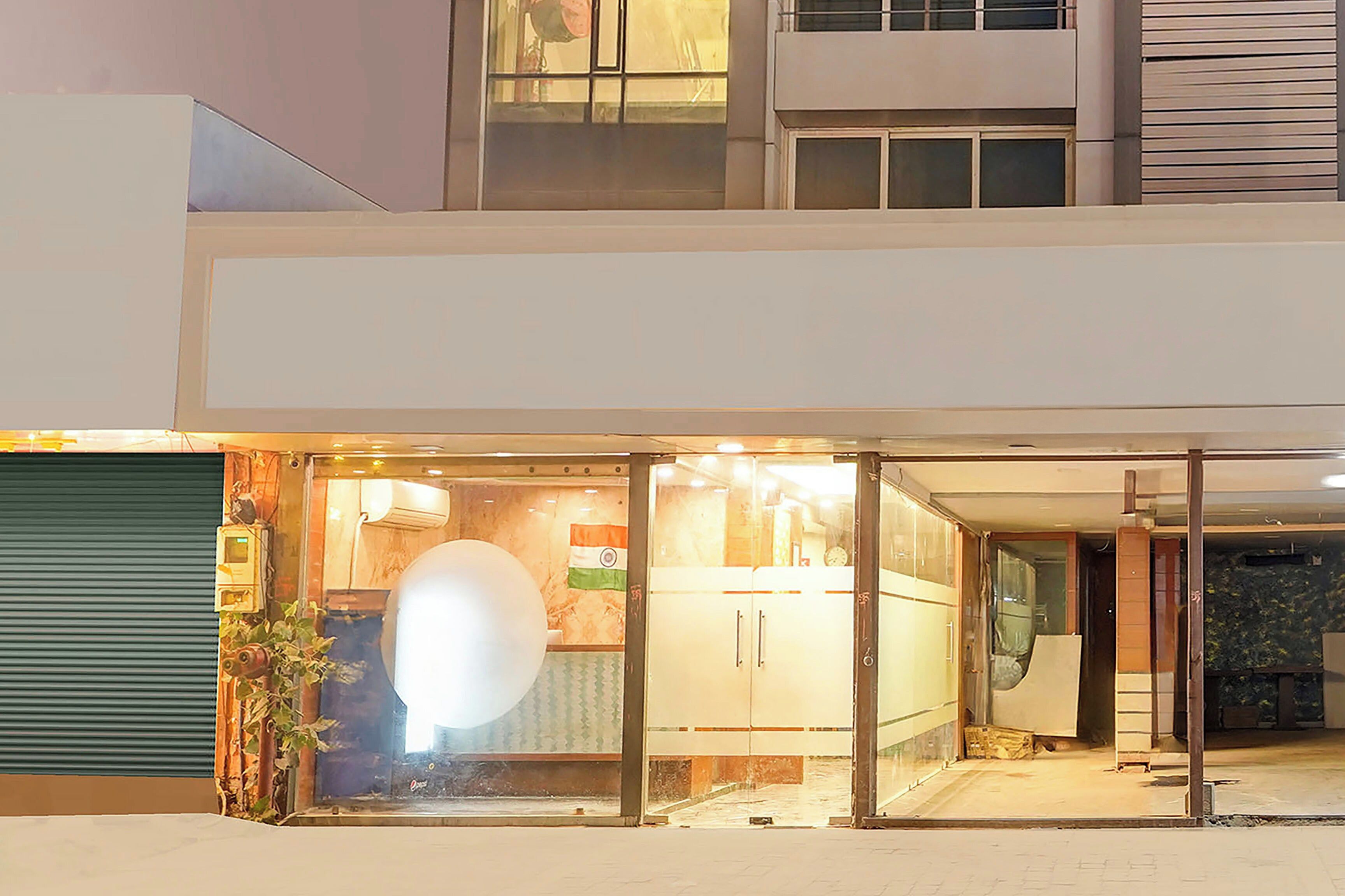 A modern building with a glass entrance, a visible kitchen area, and a green shutter door.